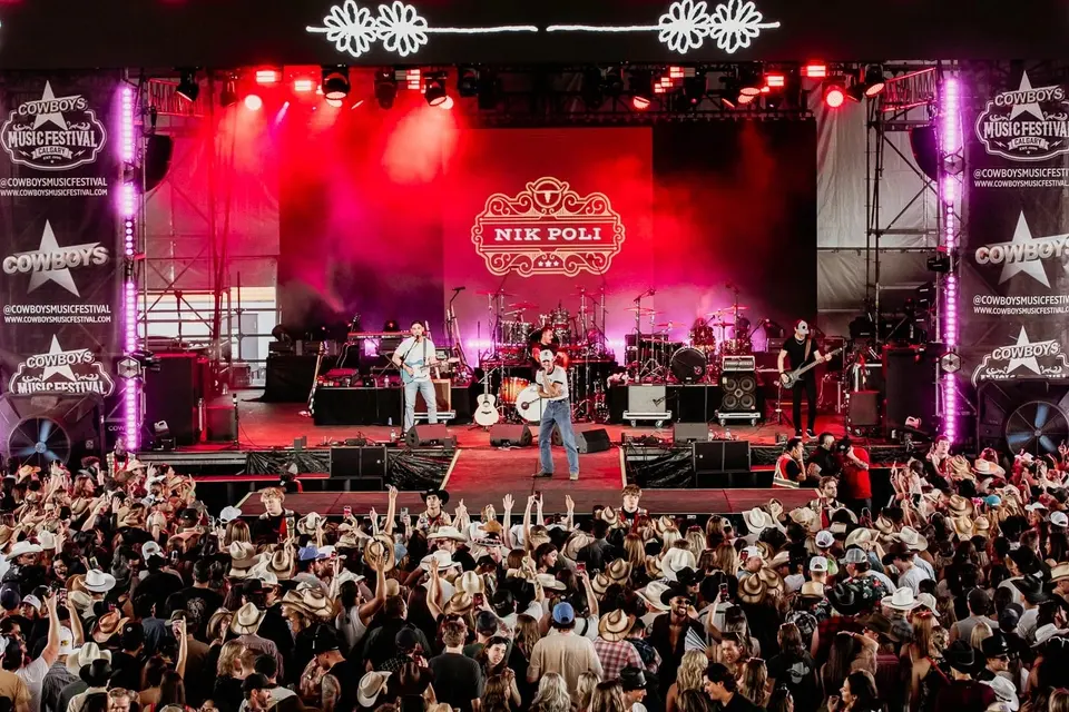 Nik Poli and band on the red-lit Cowboys Music Festival 2024 stage, the crowd in cowboy hats packed to the front