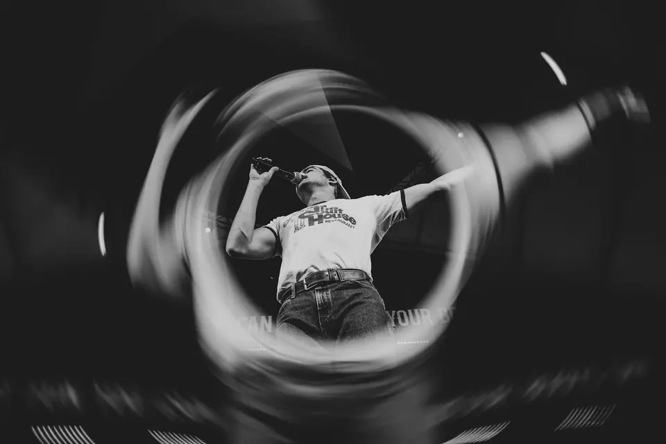 Black and white low-angle shot of Nik Poli singing, framed by a swirling lens ring