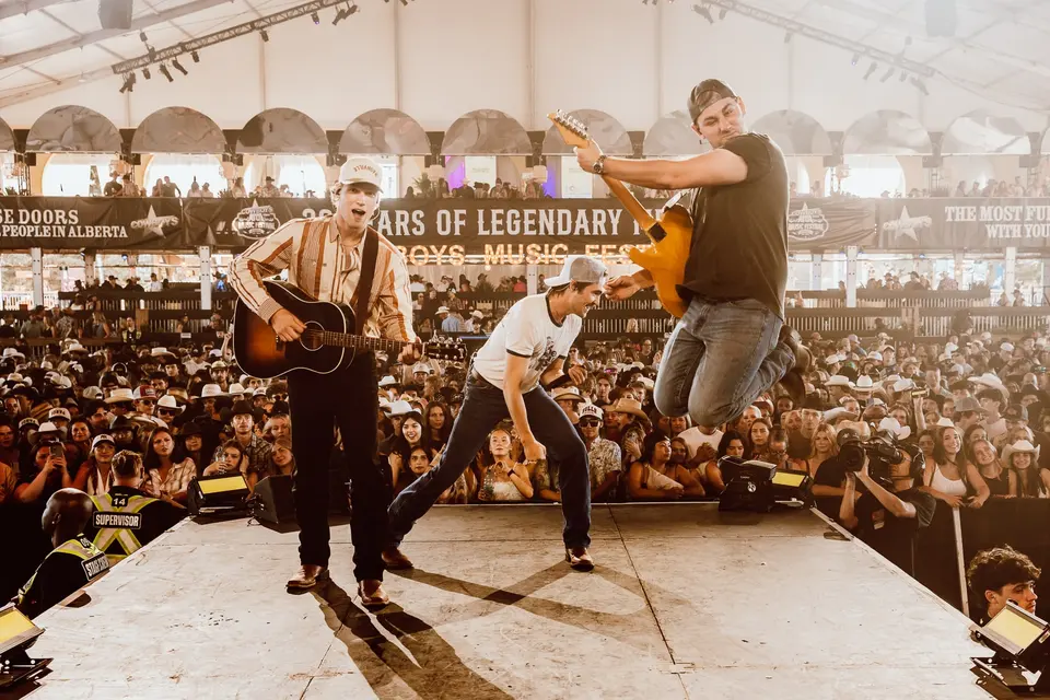 Nik Poli mid-air on stage at Cowboys Music Festival 2026, band behind him, crowd stretching back under the tent